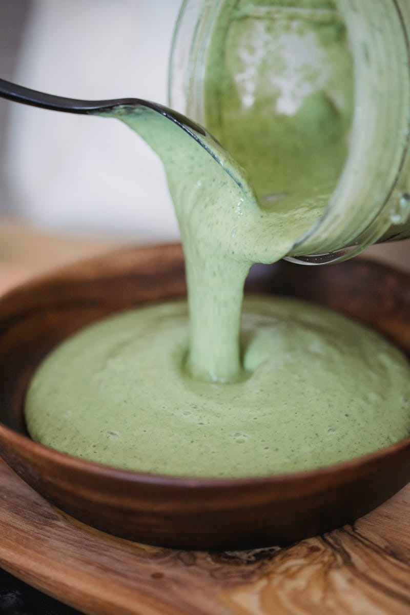 Close-up of creamy green smoothie being poured into a wooden bowl.